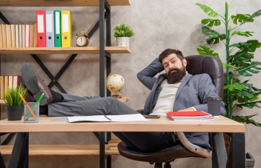 Takım elbiseli yorgun adam işten dinleniyor, bacakları masanın üstünde, dinleniyor..