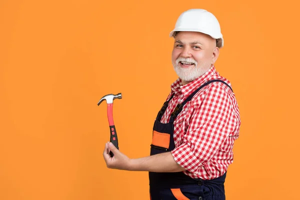happy aged man carpenter in helmet on yellow background.
