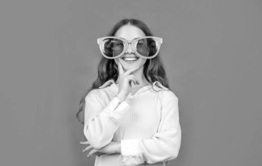 Neşeli çocuk, komik güneş gözlüklü kahverengi arka planda çene okşuyor..