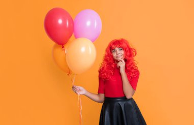 pondering teen girl with party balloon on yellow background.