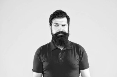 Ciddi sakallı, sarı arka planda tişörtlü, cilt bakımlı bir adam..