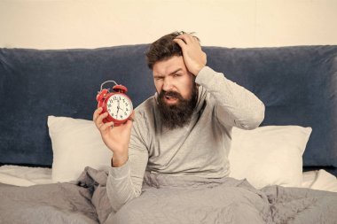 Elinde çalar saat tutan uykucu adam sabah yatağında, uyuyakalmış..