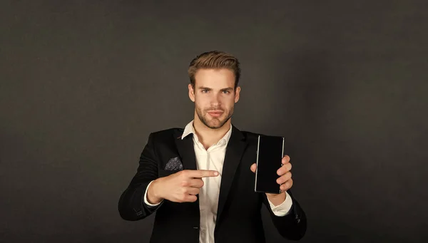 Professional manager in suit pointing finger at mobile device dark background copy space, phone.