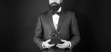 Smokinli, papyon takmış siyah arka planda hediye kutusuyla kesilmiş bir adam. Boks günü.