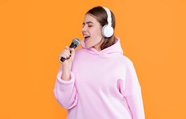 Sarı arka planda mikrofonu olan kulaklıklı mutlu genç bir kadın..