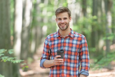 happy caucasian man with coffee wearing checkered shirt. photo of caucasian man with coffee in the forest. caucasian man with coffee outdoor. caucasian man hold coffee.