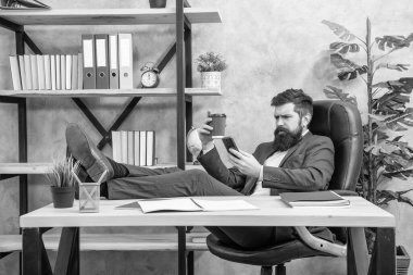 Takım elbiseli ciddi bir adam. Ofis koltuğunda rahat ol. Akıllı telefondaki mesajları oku ve kahve iç..