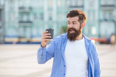 surprised guy offering coffee outdoor. guy offering coffee outside. guy offering coffee in the street. photo of guy offering coffee.
