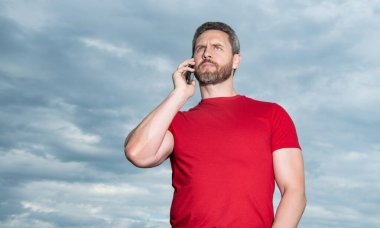 man has phone talk on sky background, conversation. man has phone talk outdoor. man has phone talk wear red tshirt. photo of man has phone talk.