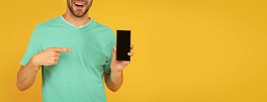 Kesilmiş adam telefon ekranını sunuyor. Adam sarı arka planda akıllı telefonu işaret ediyor. Ürün teklifi. Reklam sunumu. Boşluğu kopyala.