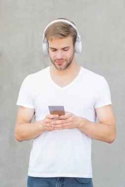 young man choose mp3 music playlist wearing white shirt. photo of man mp3 music playlist in headphones. man open mp3 music playlist. man use mp3 music playlist outside.