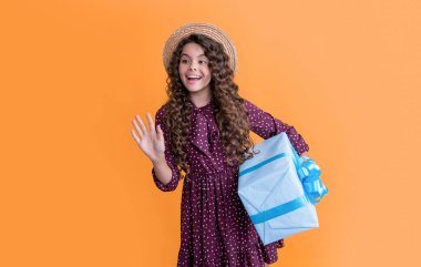 Kıvırcık saçlı hayret bir çocuk sarı arka planda hediye kutusunu tutuyor..