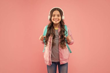 Kulaklıklı mutlu genç kız. Müzik dinle. Kablosuz kulaklık cihazı aksesuarı. Yeni teknoloji. Çocukluk gelişimi. Modern kulaklıklı, sırt çantalı bir çocuk. Online eğitim. Okula geri dön..