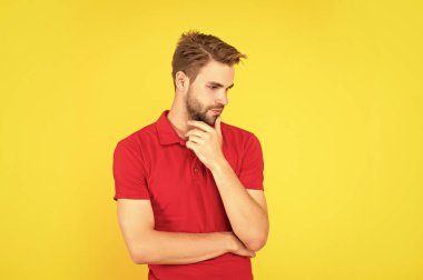 Kendine güvenen ve yakışıklı, tıraşsız adam. Erkek modası. Erkek güzelliği. Kırmızı tişörtlü bir adamın portresi. Sarı arka planda sakallı genç bir adam. saç ve sakal bakımı.