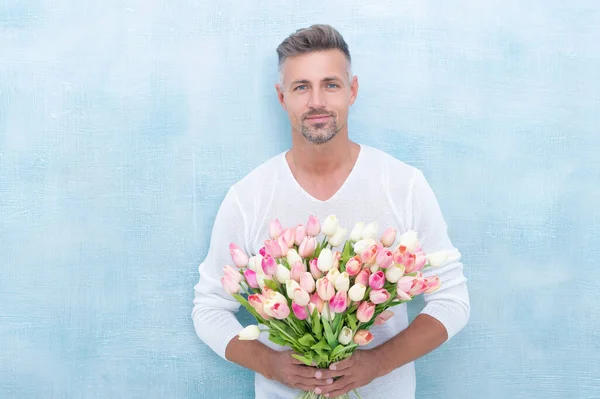 stock image mature man with spring tulips isolated on blue background. photo of man with spring tulips. man with spring tulips. man with spring tulips in studio.