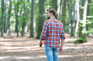 back view of walking man walk outside. walking man wearing checkered shirt for a walk. photo of walking man walk in the forest. walking man walk outdoor.