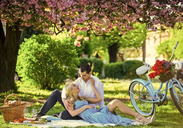 Love story. girl and man under sakura. couple in love drinking wine during romantic dinner in park. picnic of couple in love at vintage bike. family relationship and friendship. summer holiday trip.