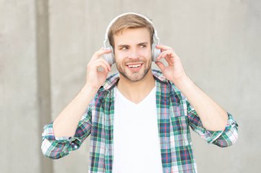 photo of glad man listening music in headphones. man listening music outdoor. man listening music outside. man listening music and wearing checkered shirt.