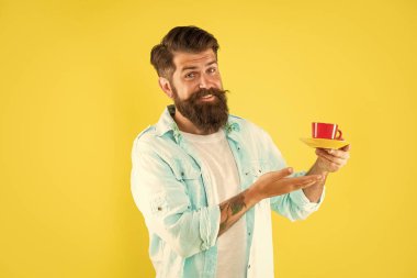 Mutlu sakallı adam sarı arka planda sabah kahvesini sunar..