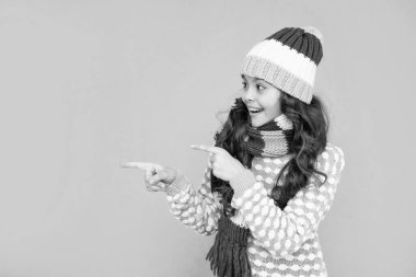 sürpriz genç kız mavi arka planda. Kalın giysiler giyen çocuk portresi. Olumlu duygularını ifade et. Kış modası. Kopya uzayı üzerinde işaret parmağı. Şapkalı ve atkılı kıvırcık saçlı çocuk..