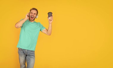 Kulaklıklı genç adam kahve içer. Müzik aşığı. Müzik dinle. Kablosuz cihaz aksesuarı. Yeni teknoloji. Modern kulaklıklı, kahve bardağıyla şarkı söyleyen adam. Online eğitim. Okula geri dön..