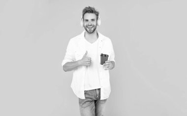 Beyaz tişörtlü mutlu adam kulaklık takıyor sarı arka planda kahve fincanı tutuyor, yaşam tarzı..