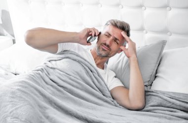 Uykulu, olgun bir adam telefonda konuşuyor. Baş ağrısı.