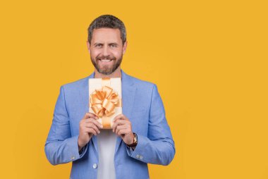 positive guy hold gift box in studio. guy with gift box for holiday. photo of guy holding occasion gift box. guy hold gift box isolated on yellow background.