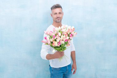 photo of man smile with valentines tulips. man with valentines tulips. man with valentines tulips in studio. man with valentines tulips isolated on blue background.