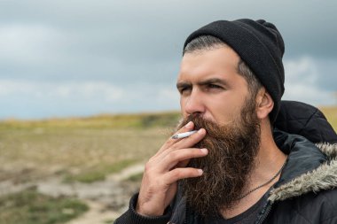 man with beard smoking cigarette, advertisement. bearded man smoking cigarette. photo of man smoking cigarette in the mountain. man smoking cigarette outdoor.