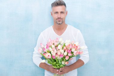 Bahar laleli yakışıklı bir adamın fotoğrafı. Bahar laleli bir adam. Stüdyoda bahar laleleri olan bir adam. Bahar laleleri olan bir adam mavi arka planda izole edilmiş..