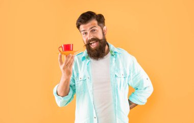 Sarı arka planda kahve fincanı tutan sakallı, olgun bir hippi..