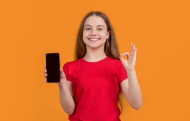 Sarı arka planda akıllı telefonu olan mutlu bir çocuk. Tamam.