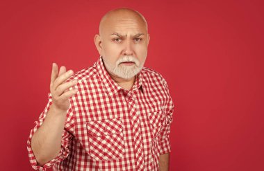 Kırmızı arka planda kareli tişörtlü kafası karışmış yaşlı bir adam..
