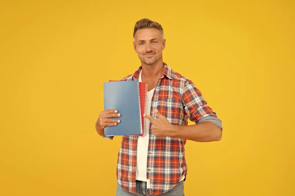 Happy guy student pointing finger at books yellow background, education.