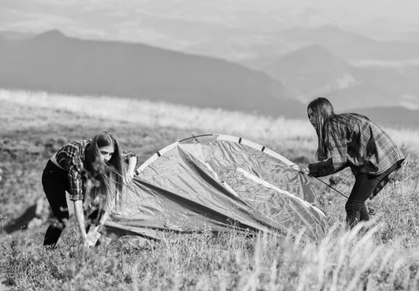 Camping trip. Helpful to have partner for raising tent. Camping skills concept. Camping and hiking. In middle of nowhere. Girls set up tent on top of mountain. Summer adventures. Temporary housing.