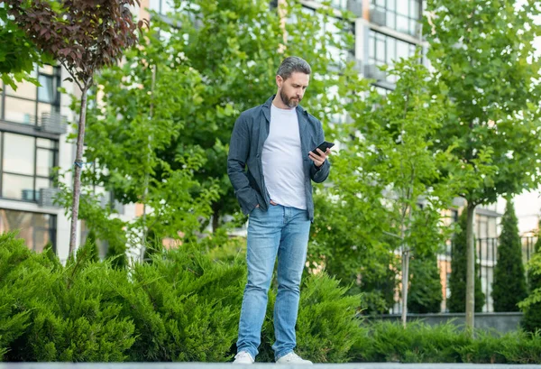 full length of man chatting on phone outdoor. man chatting on phone in the street. man chatting on phone outside. photo of man chatting on phone in hands.