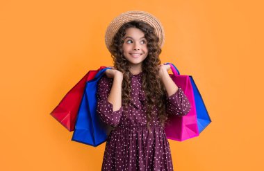 Kıvırcık saçlı pozitif kız sarı arka planda alışveriş torbaları tutuyor..