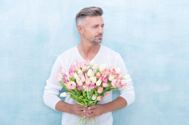 Bahar laleleri tutan adamın fotoğrafı. Bahar laleli bir adam. Stüdyoda bahar laleleri olan bir adam. Bahar laleleri olan bir adam mavi arka planda izole edilmiş..