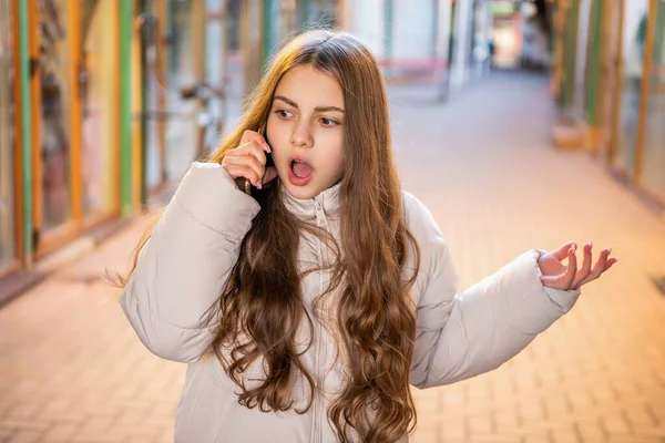 shocked teen girl having phone call in the street. teen girl having phone call outdoor. teen girl having phone call conversation. photo of teen girl having phone call outside.
