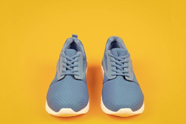 Sarı arka planda bir çift rahat mavi spor ayakkabı, spor kıyafetleri.