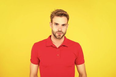 Saç ve sakal bakımı. Kendine güvenen ve yakışıklı, tıraşsız adam. Erkek modası. Erkek güzelliği. Kırmızı tişörtlü bir adamın portresi. Sarı arka planda sakallı genç adamın yüzü.