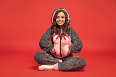 Rahat pijamalı mutlu çocuk kırmızı arka planda komik terlikler tutuyor, çocukluk..