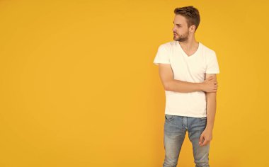 Kendine güvenen ve yakışıklı, tıraşsız adam. Erkek modası. Erkek güzelliği. Beyaz gömlekli kıllı adam. Sarı arka planda sakallı, kopyalama alanı olan genç bir adam. saç ve sakal bakımı.