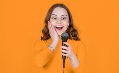 Sarı arka planda mikrofonu olan genç bir kız..