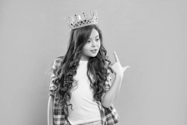 Kıvırcık saçlı bencil çocuk mavi arka planda kraliçe tacını işaret ediyor, kibirli..