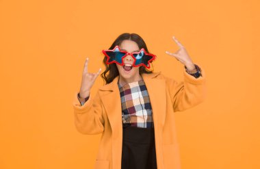 Çılgına dönüyor. Çılgın çocuk boynuzlarını gösterip el hareketi yapıyor. Deli gibi görünen mutlu kız sarı arka planda. Moda çocuğu yıldız şeklinde gözlük takıyor. Çılgın tatil havası. Okul tatili.