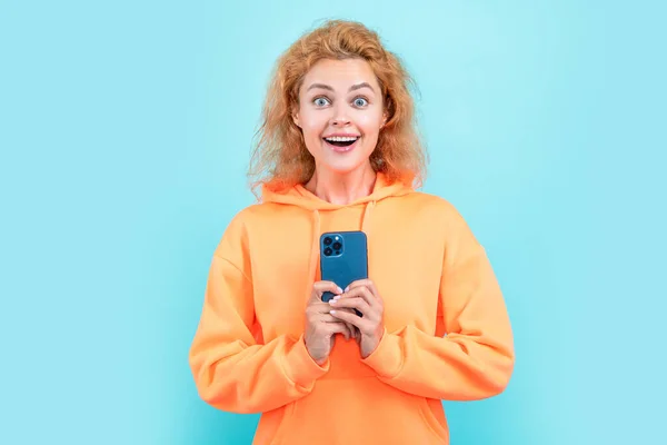 amazed redhead woman chat on smartphone on color background. woman chat on smartphone isolated on blue background. woman chat on smartphone at studio. photo of woman chat on smartphone in hoodie.