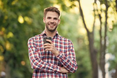 Kahve fincanıyla kareli gömlekli genç adam gülümsüyor..