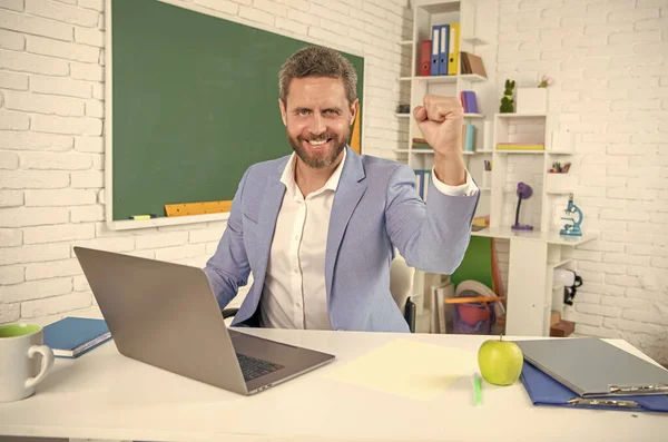 successful school teacher in classroom with computer at blackboard.